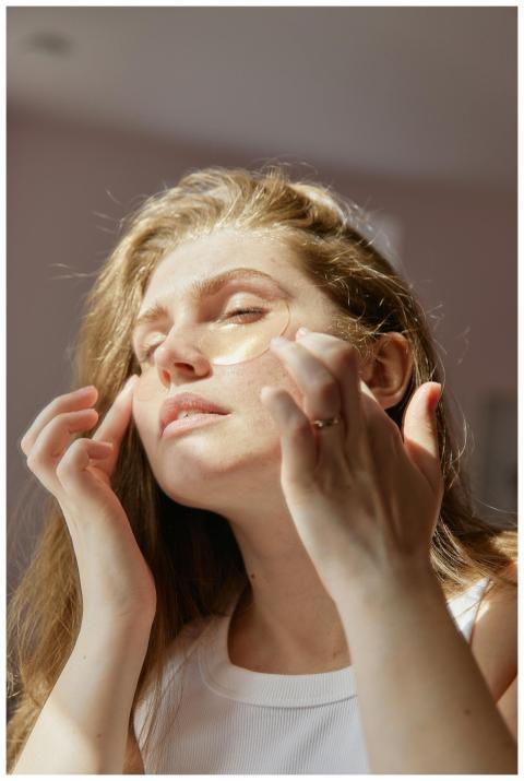 A woman gently applies under eye patches as part o
