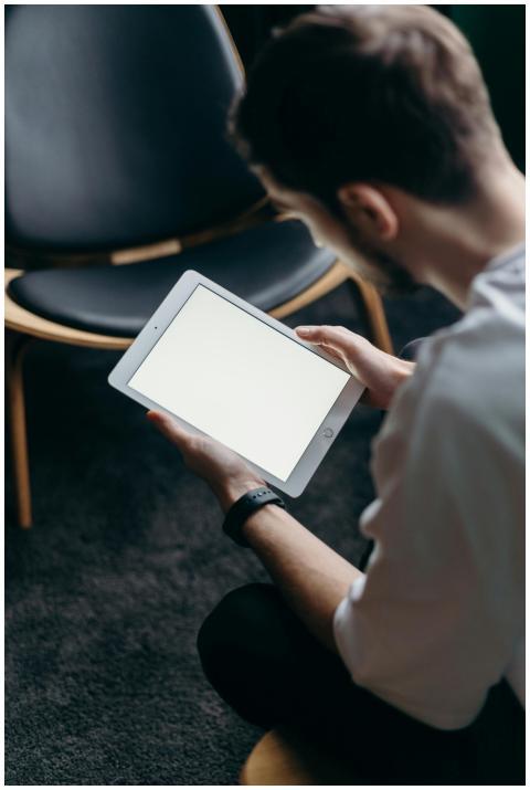 A young man seated indoors using a tablet, perfect