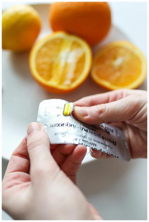 Person holding vitamin capsule with sliced oranges