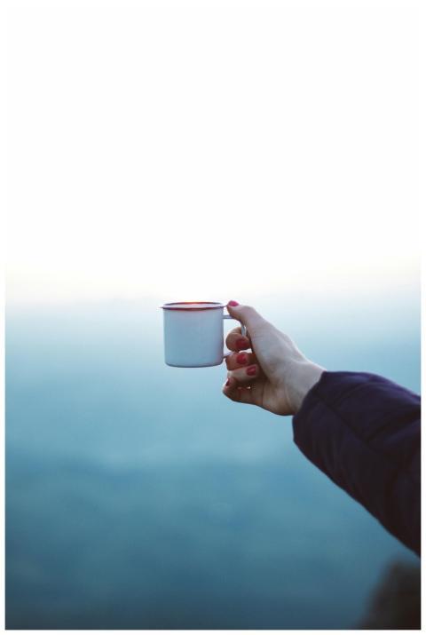 A hand extends holding a white coffee cup against