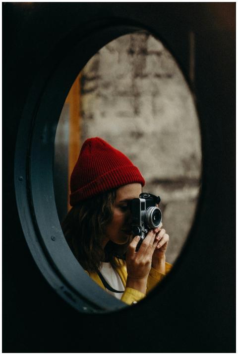 A woman in a red beanie photographs indoors with a