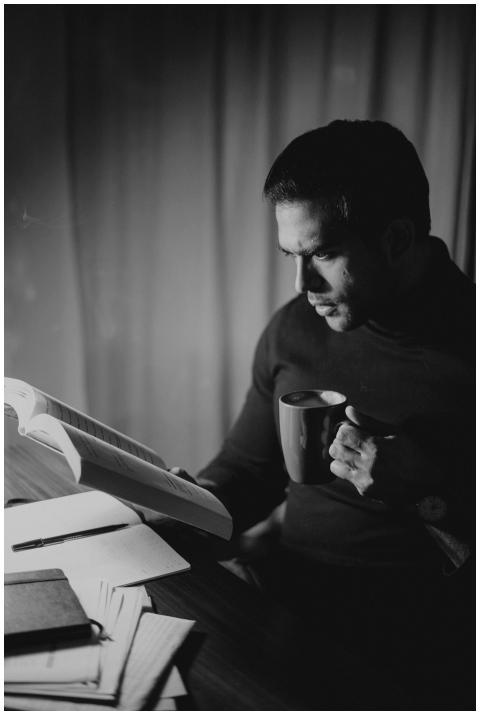 A focused man reading a book and holding a coffee