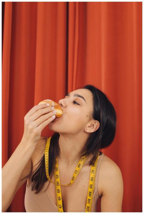 Woman eating pastry with measuring tape around nec