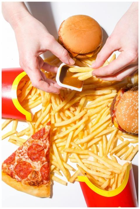 Top view of hands grabbing fries, a burger, and pi