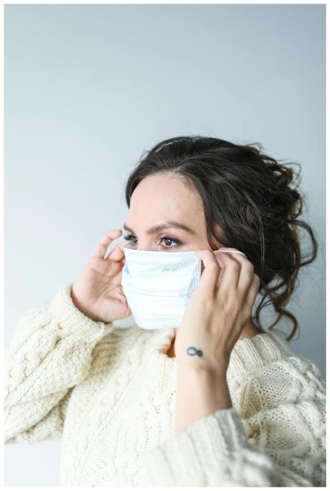 Close-up of a woman adjusting a medical mask indoo