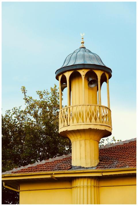 A charming yellow minaret with a metal dome agains