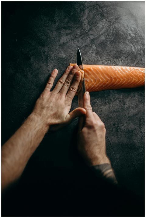 Chef expertly slicing fresh salmon on dark surface