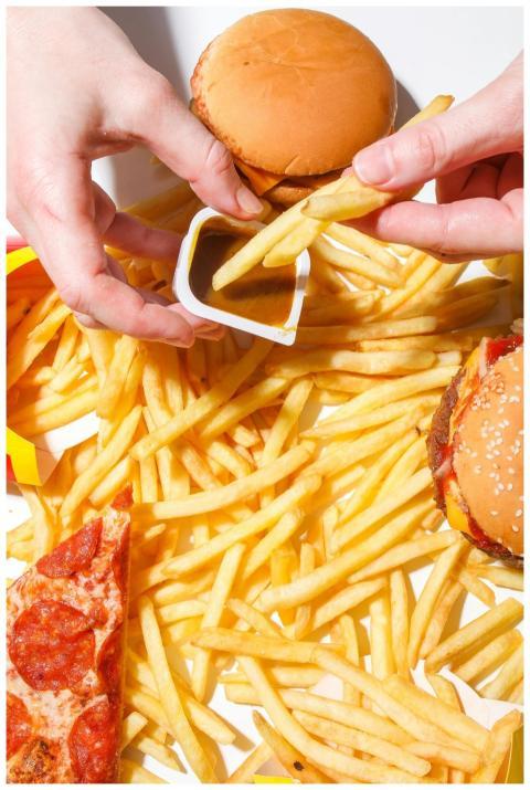Close-up of hands holding fries over burgers and p