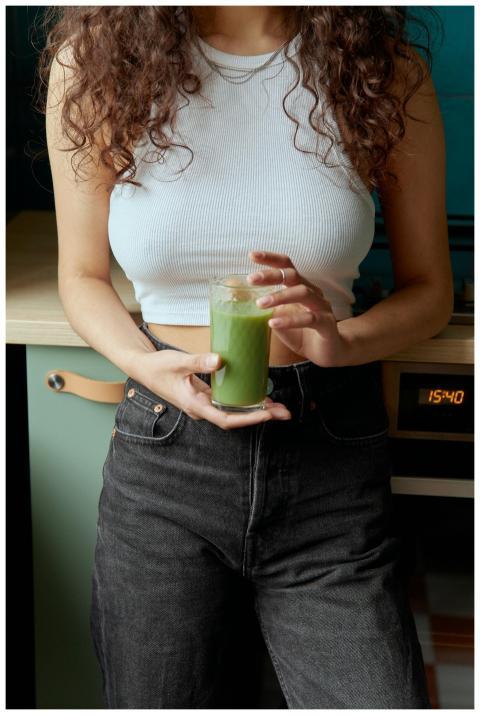 A woman indoors holding a green smoothie, showing