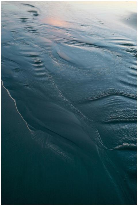 Gentle waves flowing over a sandy shore at sunset,
