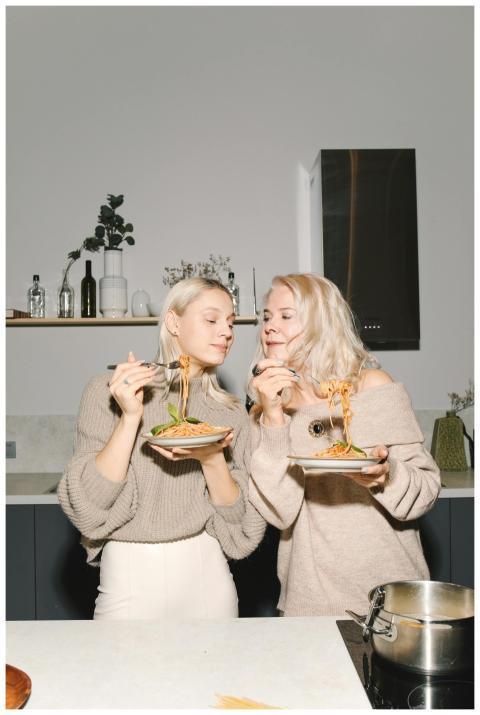 A joyful blonde mother and daughter enjoying pasta