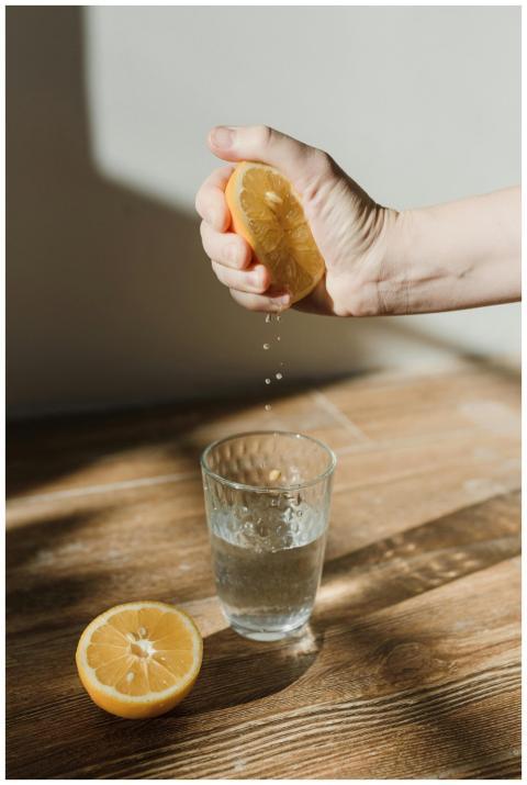 Hand squeezing a fresh lemon over a glass of water