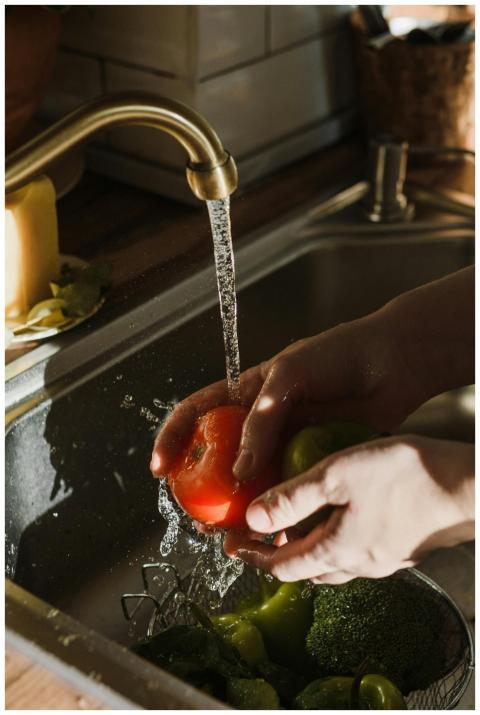 Close-up of hands washing a ripe tomato under a ki