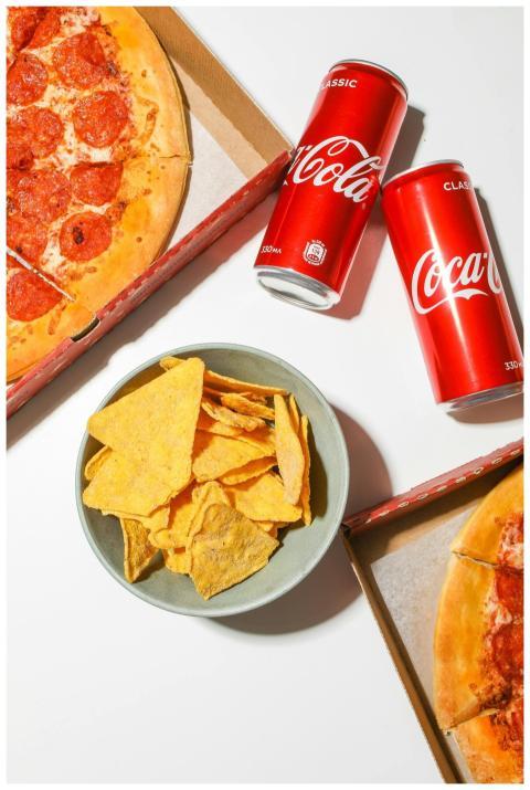 Delicious pepperoni pizza, cola cans, and chips on