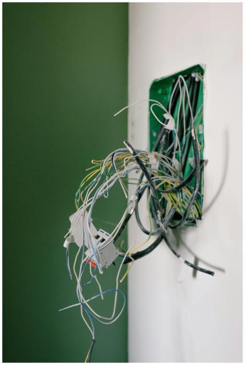 Opened power socket with various wires on white wa