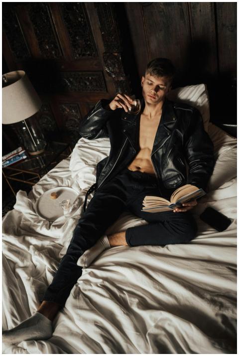 Handsome young man in leather jacket reading on be