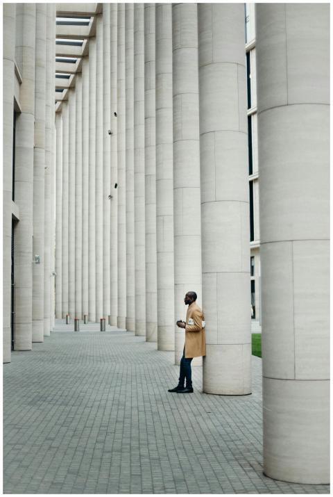 Stylish man in coat leans against columns of a mod