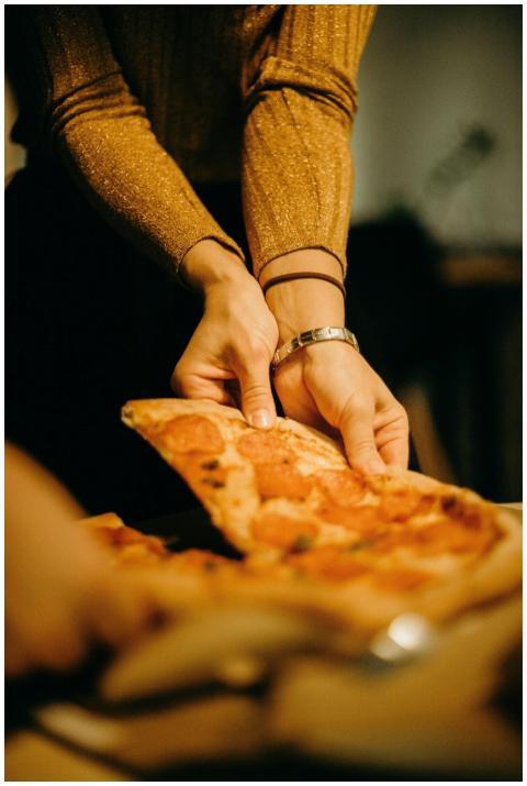 Close-up of hands serving a pepperoni pizza slice