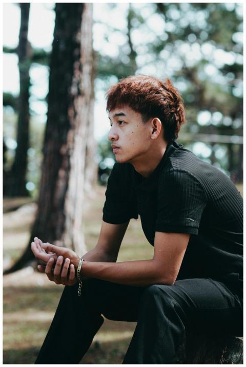 A contemplative young man sitting outdoors among t