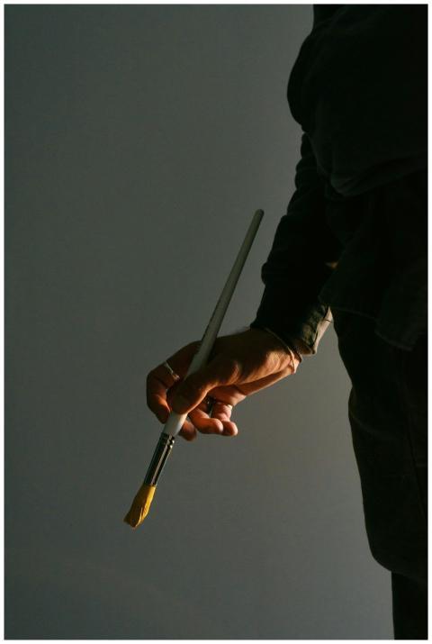 A close-up of an artist's hand holding a yellow pa
