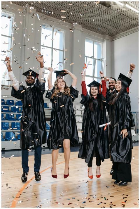 Graduates in gowns rejoice with confetti inside a