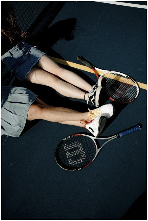 Two women resting on a tennis court with rackets,