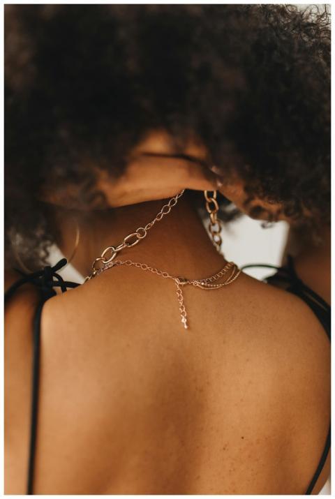 Close-up of a woman adjusting a gold necklace, hig