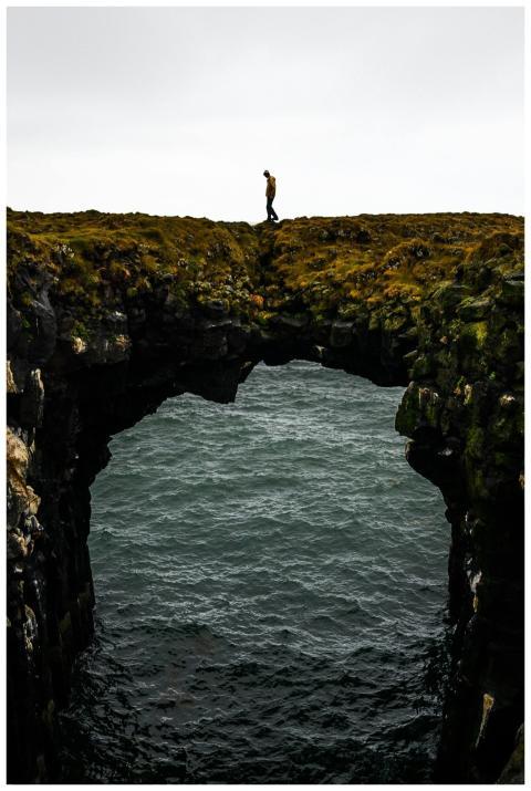 A solitary traveler walks on a rock arch over the
