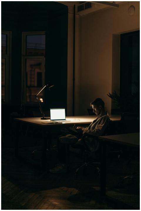 A lone man working on a laptop under dim lighting