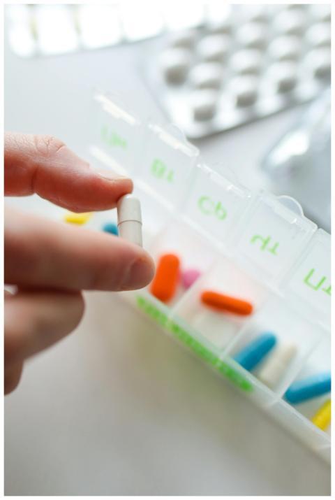 Hand holds a capsule near a colorful pill organize