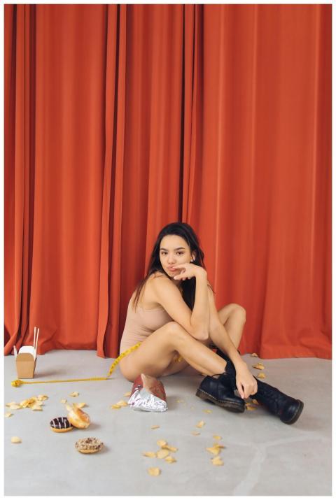 A woman sits on the floor surrounded by snacks, po