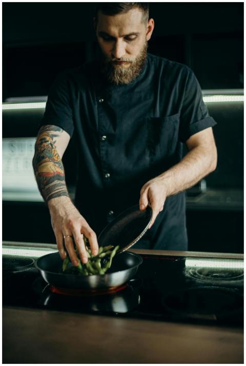 A focused tattooed chef expertly cooks a meal on a