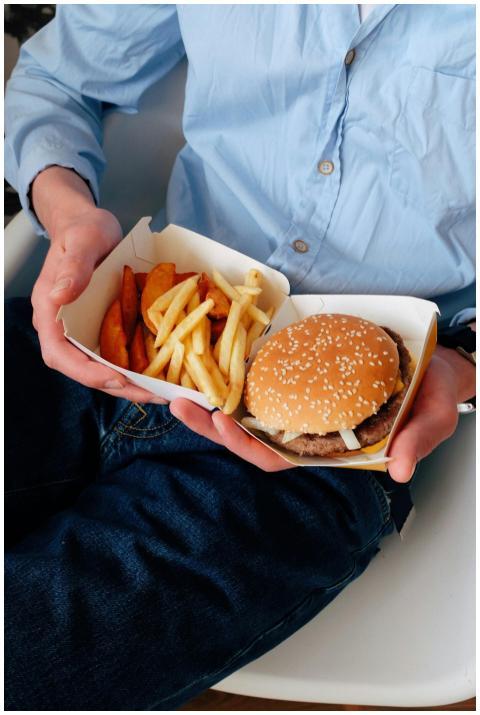 A person holds a cheeseburger and fries on their l