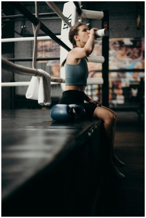 Woman boxer drinking water in gym, sitting on edge