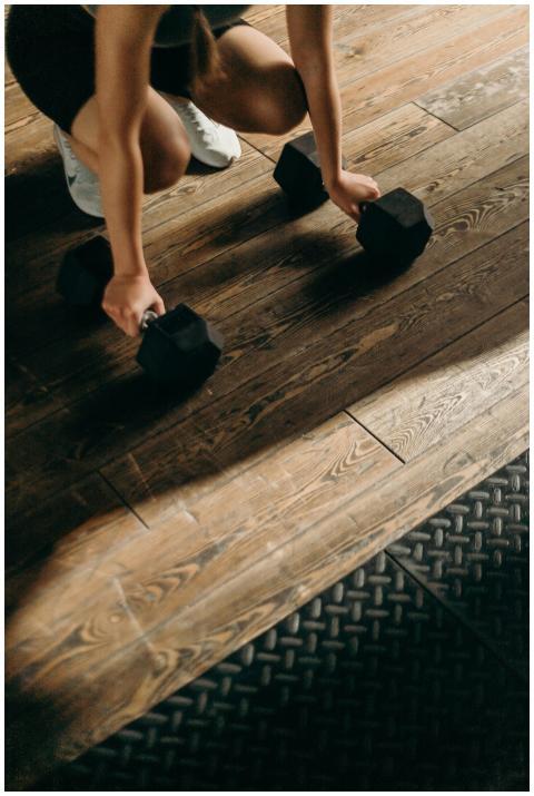 Female gym-goer in action with dumbbells on wooden