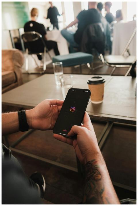 Tattooed hands hold a smartphone displaying the In