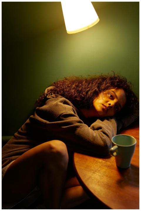 A woman sits alone at a wooden table under warm li