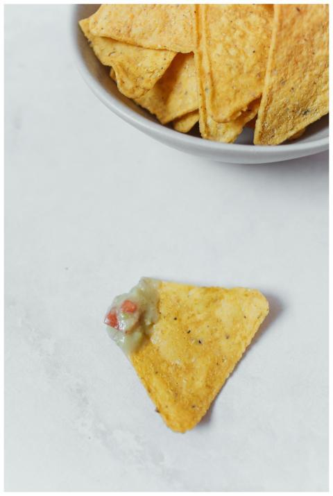 A bowl of tortilla chips with a single nacho toppe