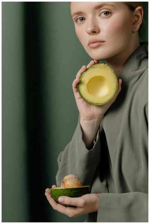 A woman in a green outfit holds a sliced avocado a