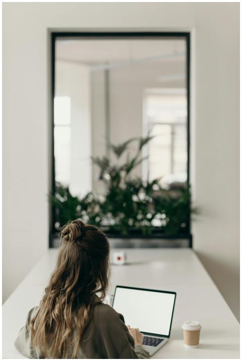 A woman with curly hair works on a laptop, facing