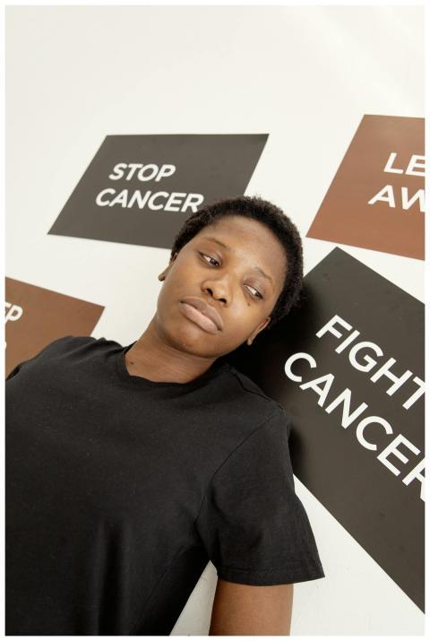 Black woman standing against a wall with cancer ad