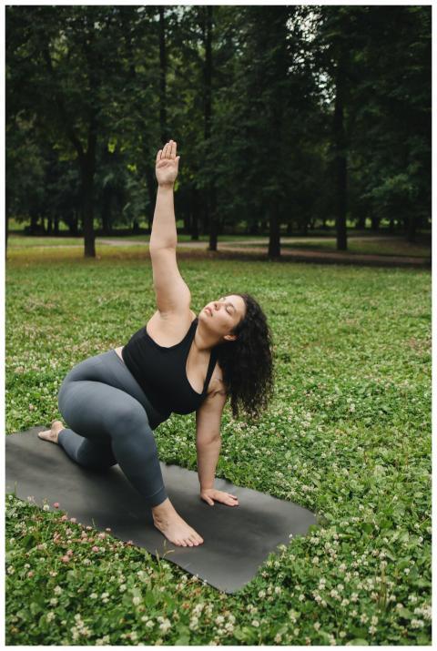 A woman practicing yoga on a mat in a park, embrac