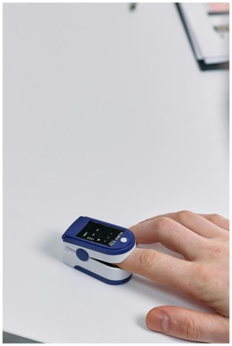 Close-up of a hand using a pulse oximeter on a whi