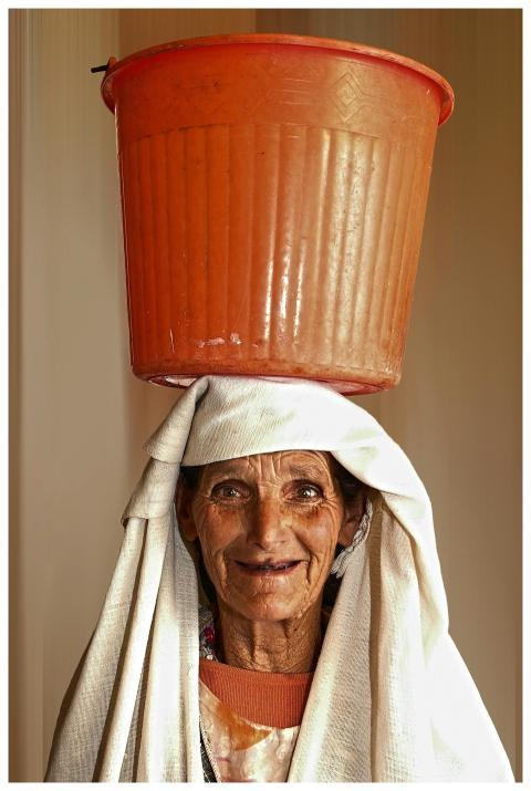 An elderly woman skillfully balances an orange buc