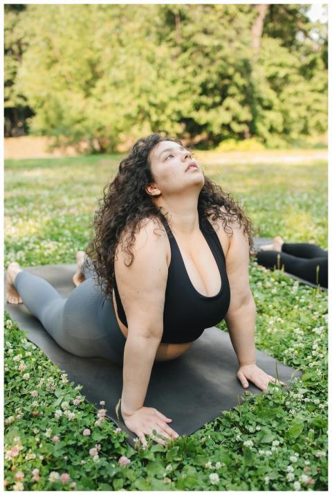 A plus size woman doing yoga on a mat outdoors in