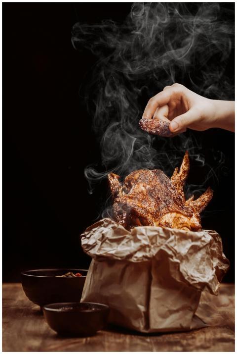 Close-up of a hand seasoning a roasted chicken, cr