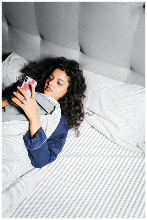 Woman in pajamas lying in bed with a smartphone, r