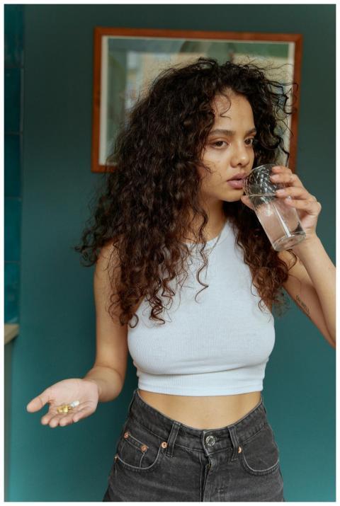 Woman with curly hair drinking from a glass and ho