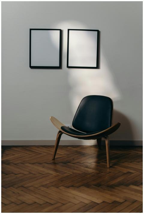 A modern armchair sits under two blank frames on a
