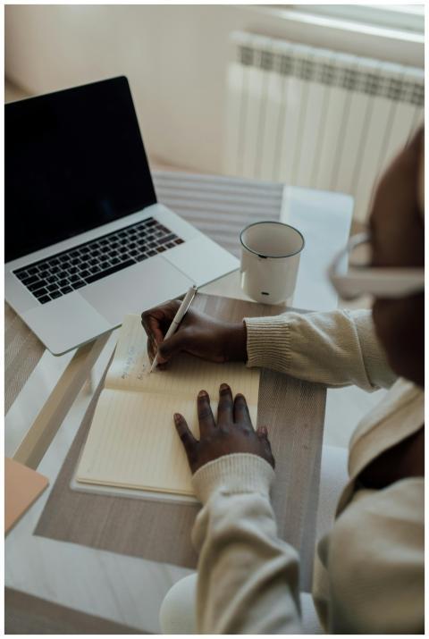 A woman writing in a notebook at a glass table wit